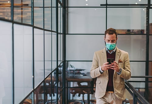 an office worker wearing a mask walks down a hallway in an office building
